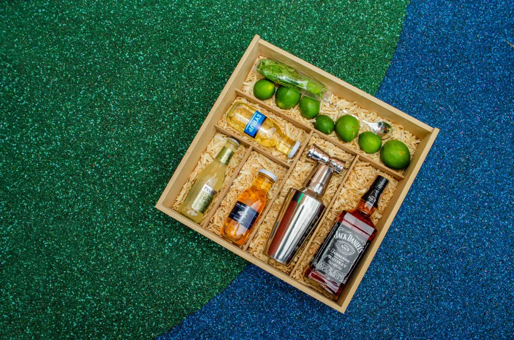 Kit de coctelería armado por Skål con whisky, coctelera, syrups y limones en caja de madera con viruta